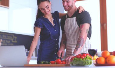 Sebze doğrayan genç bir adam ve mutfakta dizüstü bilgisayarı olan bir kadın.