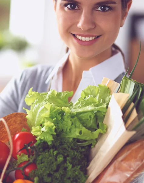 Mujer joven sosteniendo bolsa de la compra de comestibles con verduras de pie en la cocina. — Foto de Stock