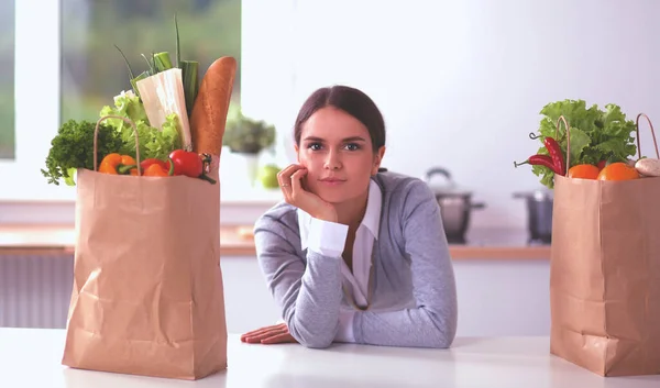 Giovane donna che tiene la borsa della spesa con verdure. In piedi in cucina — Foto Stock