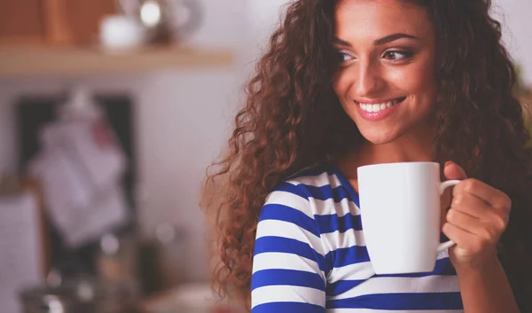 Portrait of young woman with cup against kitchen interior background. — Stock Photo, Image