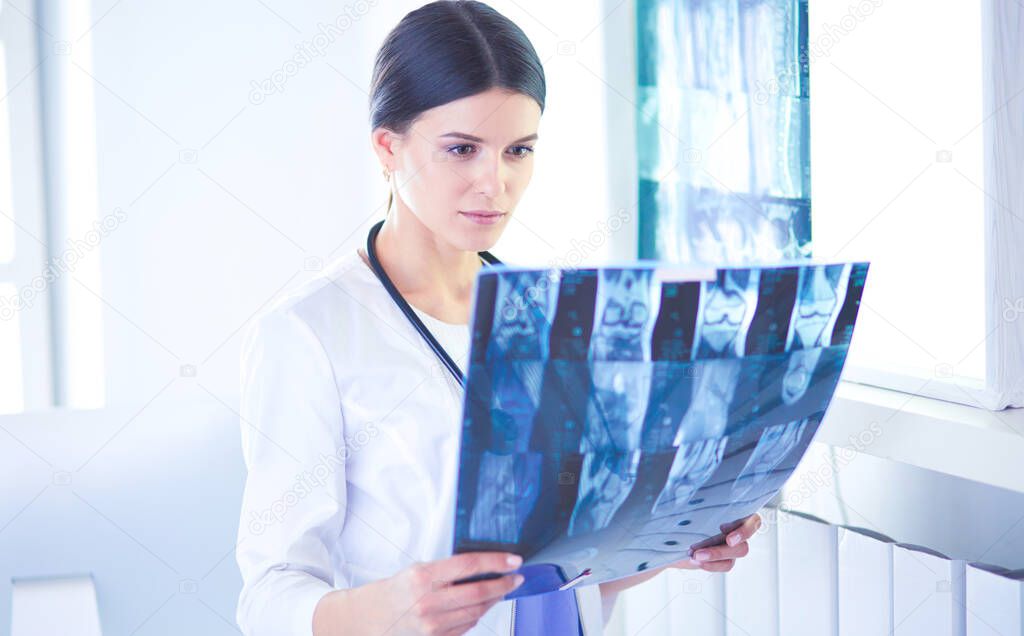 Young smiling female doctor with stethoscope looking at X-ray at doctors office