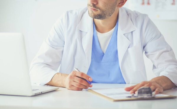 Portrait of a male doctor with laptop sitting at desk in medical office