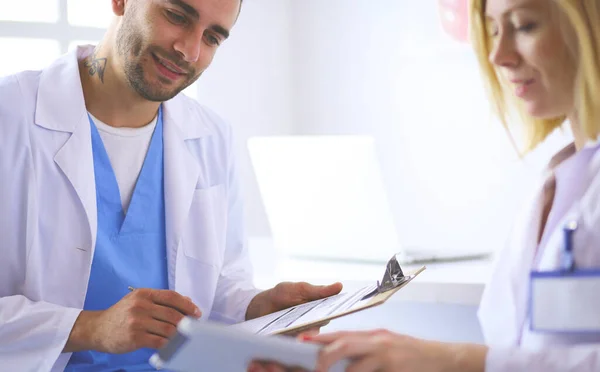 Médico bonito está conversando com jovem paciente do sexo feminino e fazendo anotações enquanto está sentado em seu escritório — Fotografia de Stock