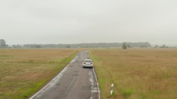 AERIAL: Cirkelen rond elektrische auto rijden over de weg in de Duitse natuur op mistige bewolkte dag — Stockvideo