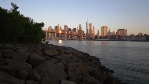 MOCIÓN LENTA: Centro de Manhattan Vista cerca del agua con el puente de Brooklyn en la hermosa salida del sol en verano Agua, Mañana — Vídeo de stock