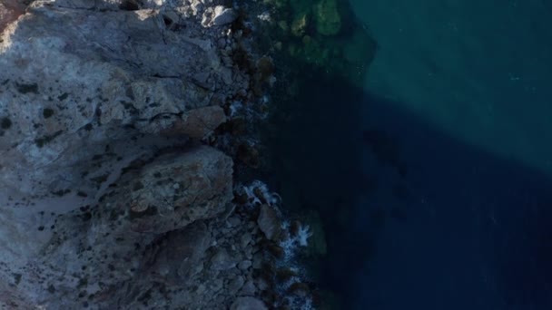 Langzame overhead top down antenne langs de generieke Rocky Coast met turkoois water en golven crashen op rotsen op Grieks eiland bij zonsondergang — Stockvideo