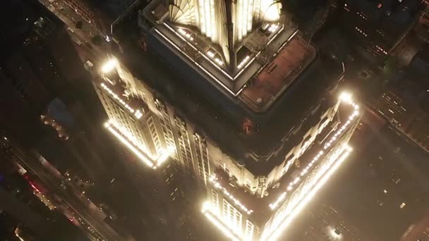 AÉRIAL : Gros plan épique de l'Empire State Building au-dessus éclairé avenues parallèles et jonctions condominiums résidentiels et immeubles de bureaux dans Midtown Manhattan, New York City la nuit — Video