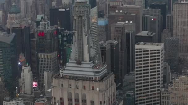 AERIAL: Olhar épico sobre o Empire State building em Manhattan cercado por arranha-céus em movimentada Cidade em dia nublado — Vídeo de Stock