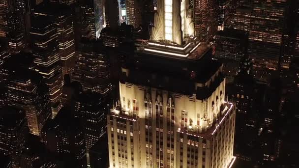AERIAL: Círculo de tirar o fôlego sobre o icônico Empire State Building acima iluminado avenidas paralelas e junções condomínios residenciais e edifícios de escritórios no centro de Manhattan, Nova York à noite — Vídeo de Stock