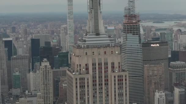 AERIAL: Olhar épico sobre o Empire State building em Manhattan cercado por arranha-céus em movimentada Cidade em dia nublado — Vídeo de Stock