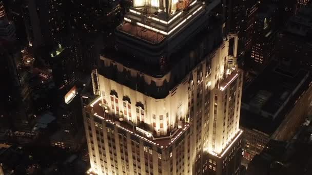 AERIAL: Häpnadsväckande flygning över den ikoniska Empire State Building ovan lyste upp parallella avenyer och korsningar bostäder och kontorsbyggnader i Midtown Manhattan, New York City på natten — Stockvideo