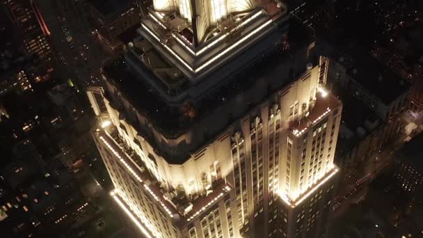 AERIAL: Epic närbild heli skott av imperium statsbyggnad ovan lyste upp parallella avenyer och korsningar bostäder bostadsrätter och kontorsbyggnader i Midtown Manhattan, New York City på natten — Stockvideo