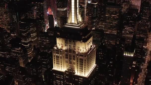 AERIAL: Εκπληκτική θέα το εμβληματικό Empire State Building άναψε παράλληλες λεωφόρους και διασταυρώσεις κατοικίες και κτίρια γραφείων στο Midtown Manhattan, Νέα Υόρκη τη νύχτα — Αρχείο Βίντεο