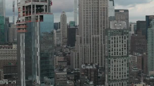 AERIAL: Flying upp Empire State byggnaden i Manhattan omgiven av skyskrapor i upptagen stad på molnig dag — Stockvideo