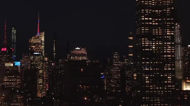 AERIAL: Fantastisk vidsträckt utsikt över den ikoniska Empire State Building försvinner bakom bostadslägenheter och kontorsbyggnader i Midtown Manhattan, New York City på natten — Stockvideo
