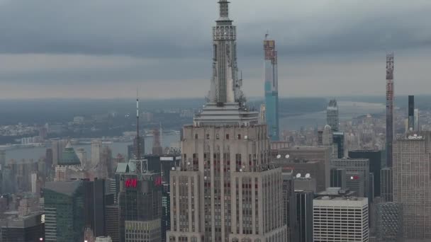 AERIAL: Epic look over the Empire State building in Manhattan surrounded by rascacielos in busy City at cloudy day — Vídeo de stock