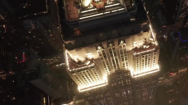 AERIAL: Dech beroucí let nad ikonickou Empire State Building nahoře osvětlil paralelní cesty a křižovatky obytných bytů a kancelářských budov v Midtown Manhattan, New York City v noci — Stock video