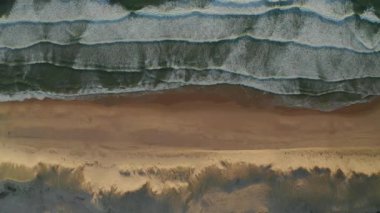 Kum tepeleri ve dalgaların beyaz köpüklerle çarpıştığı güzel sahilin geniş manzarası, Kuşlar Gözü Manzarası 'ndan aşağı doğru havadan aşağıya doğru, yavaş yanlamasına