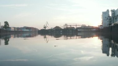 Nehirde yüzen boş bir cam şişe Port Alanı ve arka planda konteynırlar, Sabah erken saatlerde suyun üzerinde alçak hava uçuşları güneş ışığı yansımaları