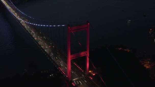 Pont du Bosphore rouge à Istanbul la nuit avec la circulation automobile dans la ville, établissant une inclinaison vers l'arrière aérienne — Video