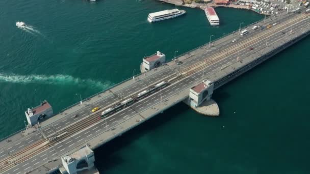İstanbul 'da boğaz üzerinden Galata Köprüsü' nden geçen toplu taşıma tramvayı treni, su üzerinde botlar, alçak açılı manzaralı havadan çekim — Stok video