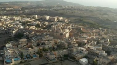 Malta Adası 'nda Bej ve Kahverengi Kum Rengi' nde küçük Akdeniz Kasabası 'nın ortasındaki kilise, Hava Dronu Perspektifi, Dolly ileri
