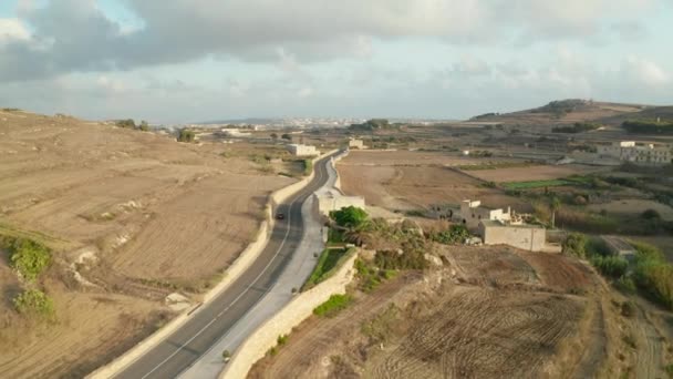 Single Red Car οδήγηση σε άδειο δρόμο μέσα από την αγροτική μεσογειακό τοπίο στο Gozo Island, Μάλτα, Σκηνικό Εναέρια ακολουθήσει tracking πυροβόλησε dolly προς τα εμπρός — Αρχείο Βίντεο