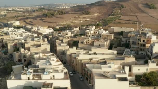 Straße durch kleine Stadt auf Gozo, Insel Malta mit Autoverkehr zwischen beige und braun gefärbten Häusern, Luftaufnahme von oben, Dolly vorwärts — Stockvideo