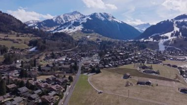 İsviçre Alpleri karla kaplı Gstaad köyünü görüntüleyen hava manzarası, parlak güneş ışığı ve geniş vadi manzarasıyla yıkanmış dağ manzarasını vurguluyor..