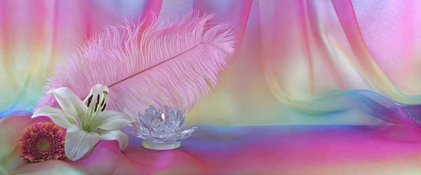 Feminine Holistic Background - pink feather, white lily, glass lotus candle and pink flower head on left with rainbow chiffon behind and copy space to the right, ideal for a website banner