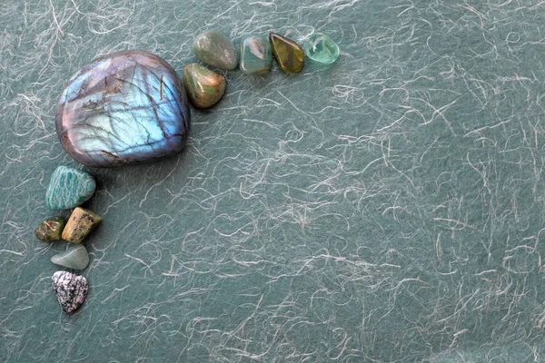 Healing Labradorite and green crystal selection background - arranged in the left corner providing copy space a large shimmering labradorite polished stone and 10 other semi-precious stones