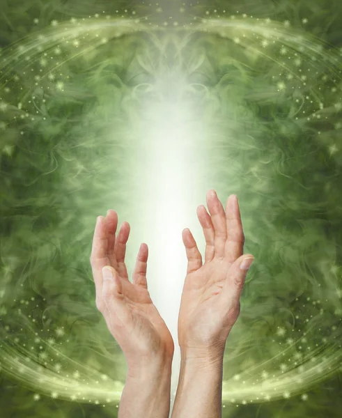 Sending Heart Chakra Healing Energy - female hands reaching up sending energy against a shaft of white light a green ethereal energy flowing sparkling background with copy space
