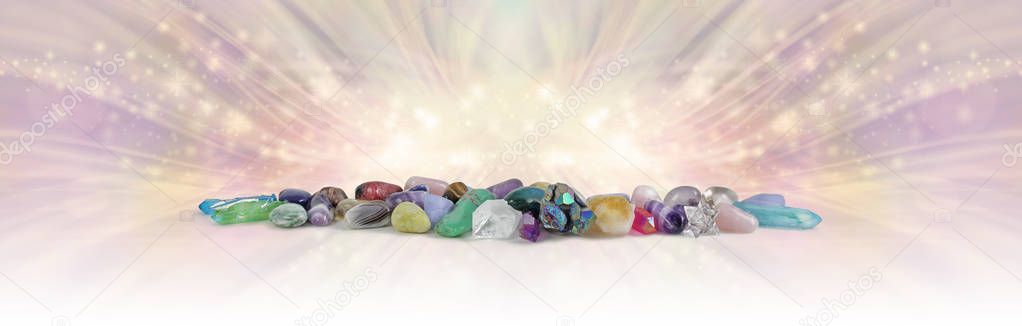 The Magical Energy of Earth's Crystals - wide row of different coloured healing stones and terminated quartz against radiating energy flowing outwards with copy space