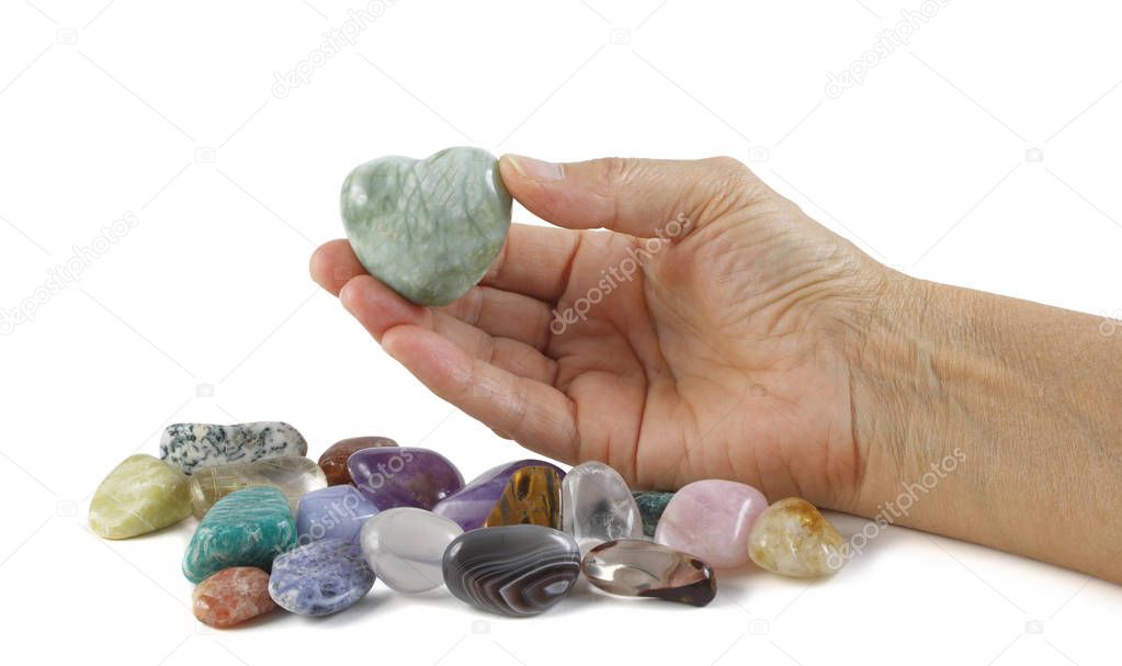 Crystal healer holding green puff heart stone - female hand offering a heart shaped crystal with a selection of other tumbled healing stones isolated on white background