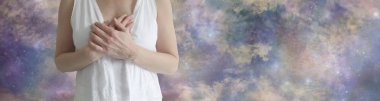 Blessed Be Goddess Gratitude banner - female torso in white robes with hands laid on chest against a wide multicoloured complex ethereal sky scape with copy space clipart