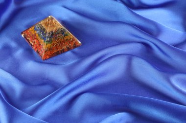 Kobalt Mavi İpek arkaplanındaki Orgone Piramidi - ya da sol üst köşede yedi çakra katmanı gösteren ve nazikçe dalgalanan kraliyet mavi ipek arka planda oturan