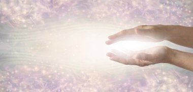 The humble hands of a light worker sending healing energy -  female parallel hands with white light between against a wide ethereal energy formation background with space for copy clipart