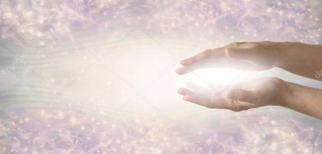 The humble hands of a light worker sending healing energy -  female parallel hands with white light between against a wide ethereal energy formation background with space for copy