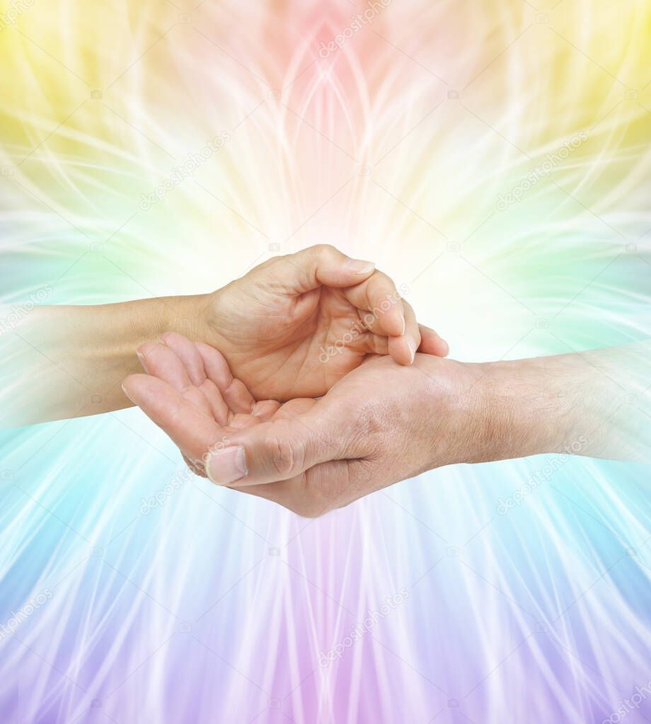 Our energies together are a formidable force - female hand cupped over a male cupped hand against a rainbow coloured symmetrical outwardly flowing energy formation background with copy space                             