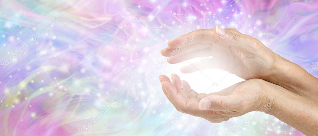 Sensing Awesome Metaphysical Energy Field between hands - female cupped hands with white healing energy against a colourful blue purple green sparkling chaotic background with copy space 