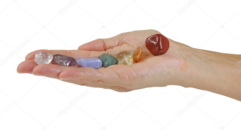 Holding Seven Chakra Healing Stones - open flat female hand with seven tumbled crystals neatly balanced in a row isolated against a white background with copy space