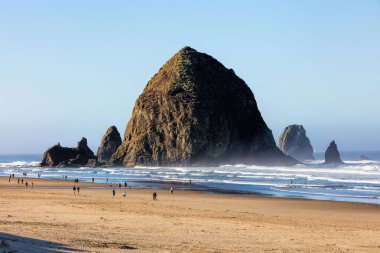 Oregon sahilinde sular çekildiğinde insanlar saman yığını kayasının yanında yürür..