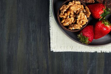 Sağlıklı çilek, fındık ve tohum omleti içeren bir kap, sağda siyah bir masada beyaz bir bez üzerinde gruplanmış, fitness gıda konsepti, vejetaryen yemeği, vejetaryen yemeği, koyu yiyecek.