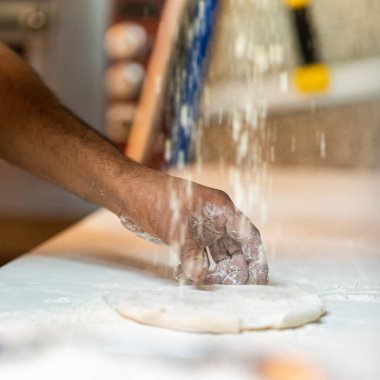 Şefin elleri hamurun üzerine un püskürtüyor. Hamur yoğurmak. Mutfak şefinin önlüğündeki erkek aşçı hamurun üzerine un püskürtüyor.