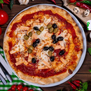 Lezzetli sıcak pizza, somon, domates ve ahşap masada yenmeye hazır farklı baharatlar.