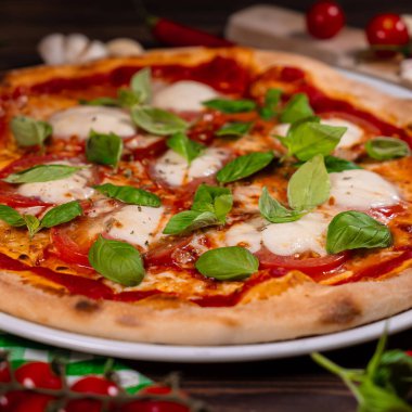 Domatesli Caprese pizzası, mozzarella ve açık gri masada fesleğen.