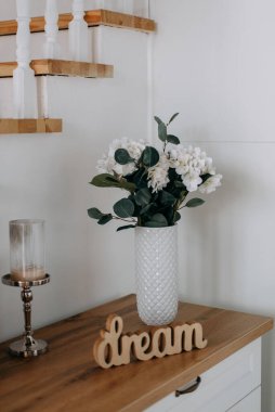 Altın çerçeveli bir vazoda beyaz ortanca çiçekleri ve Provence 'ın içinde mumlar. beyaz tahta çekmeceler ve bir merdiven.