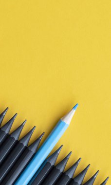 Bir sıra siyah kalem ve sarı arka planda bir mavi kalem.