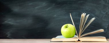 Yeşil elma bir kitabın üzerinde yatıyor. karatahta arka planı