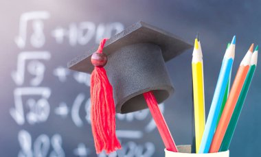 Okul yönetim kurulunun arka planında kalem üzerine mezuniyet şapkası